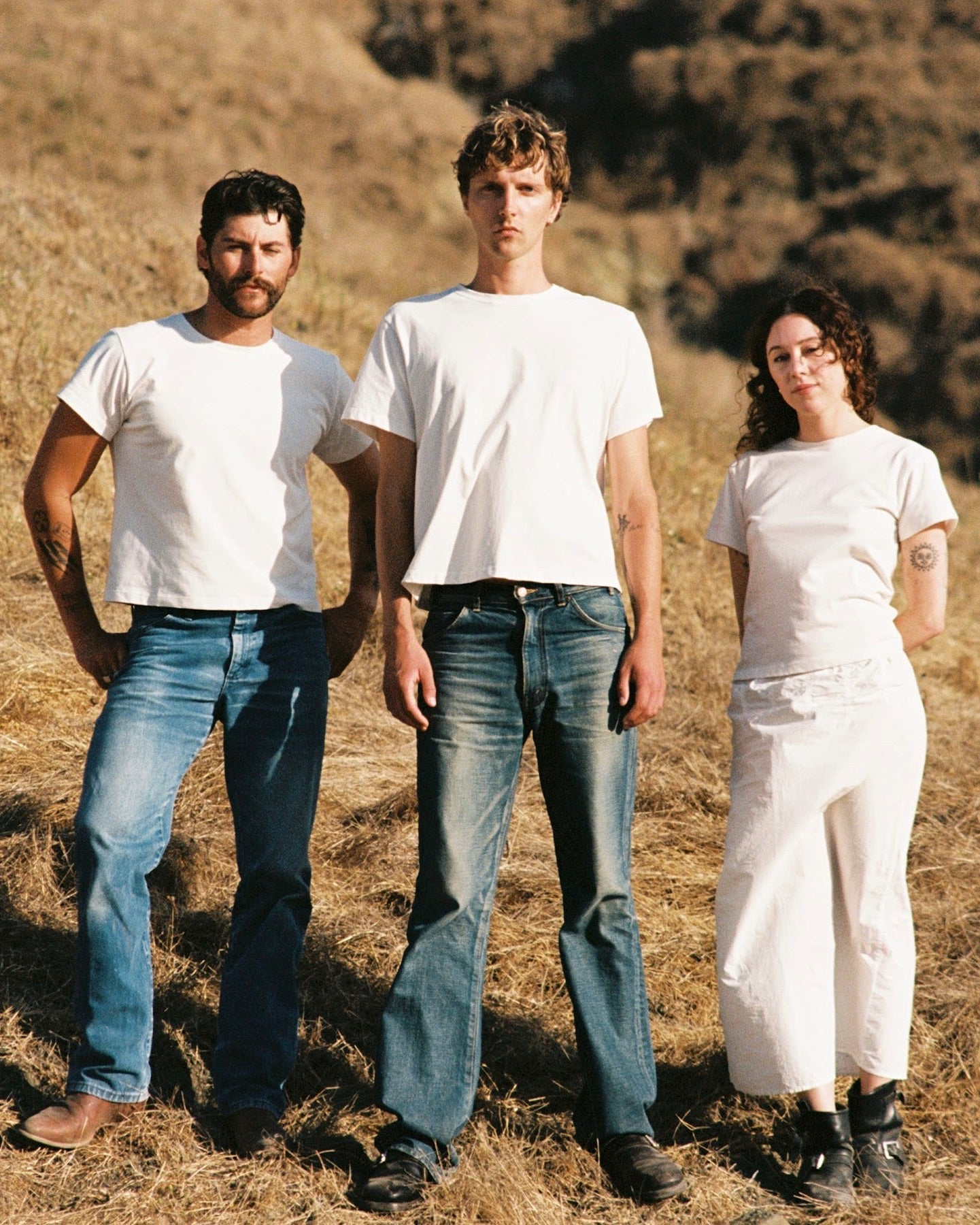 Three people standing in a field with dry grass and hills in the background
